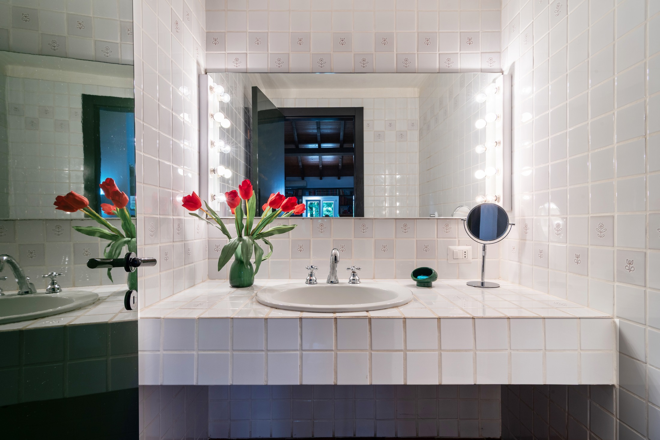 The vintage bath — Hollywood lights, tulips, the library beyond